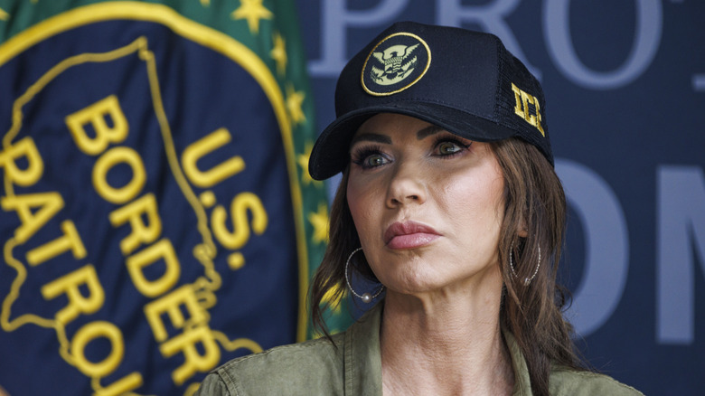 Kristi Noem in a large blue trucker hat with "ICE" on the side