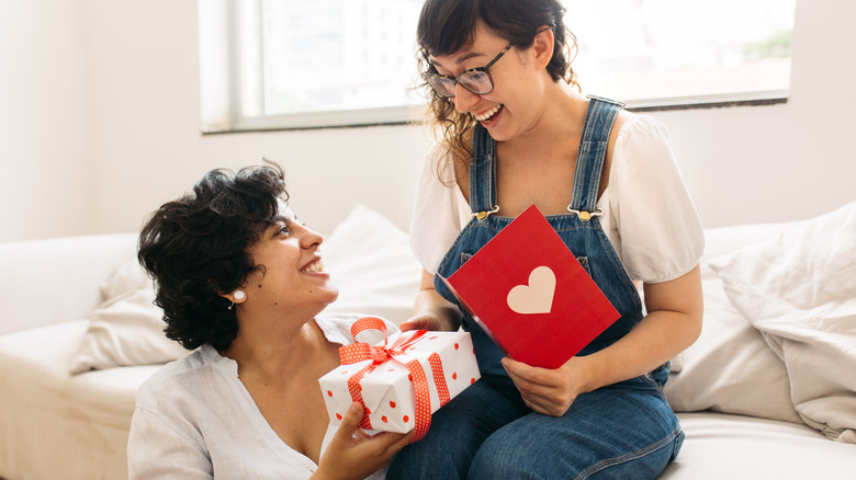 A woman kissing a man on the forehead while he presents her with a bouquet of red roses
