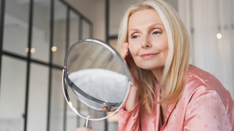 Women applying makeup in a small mirror wearing a pink robe