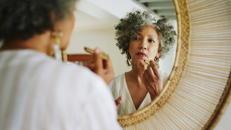 Women with curly grey hair applying makeup in a bamboo mirror