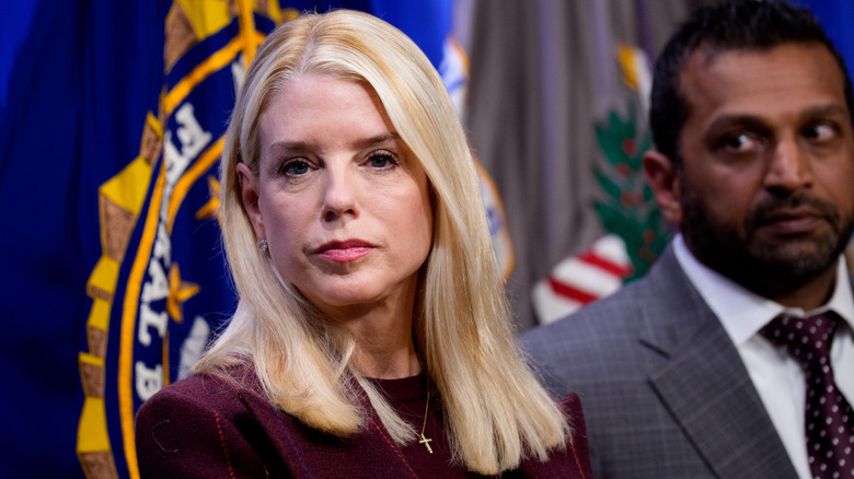 Pam Bondi with shoulder-length hair looking into the camera with Kash Patel behind her