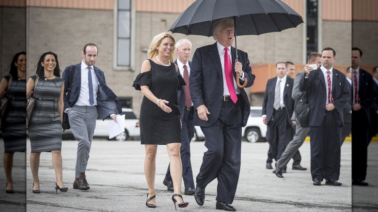 Pam Bondi walks outside next to Donald Trump who is holding an umbrella over himself