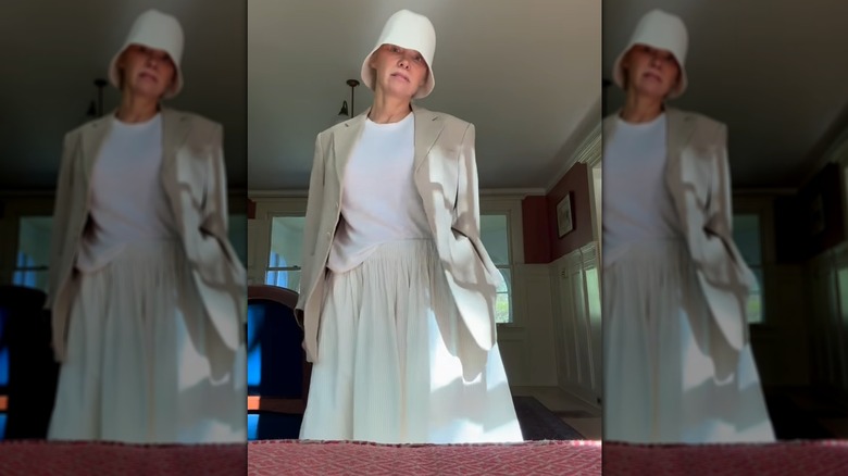 Still of Pamela Anderson showing off a breezy white outfit and cloche-style hat