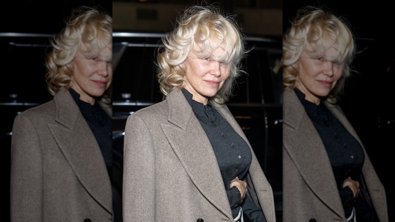 Pamela Anderson wearing a black shirt and brown blazer with short hair