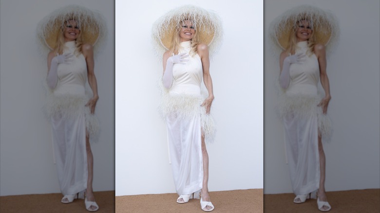 Pamela Anderson in a big hat and a white dress with white heels