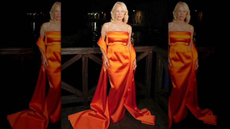 Pamela Anderson in an orange dress with a long orange shawl at an event