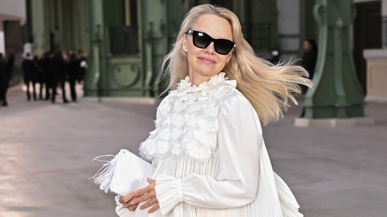 Pamela Anderson photographed with a small smile, sunglesses, and her hair flipping over her shoulder