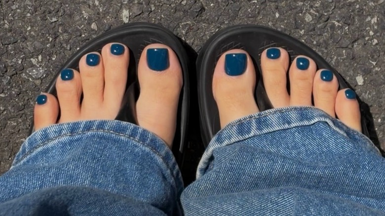 A woman wearing blue jeans and black sandals with a dark blue pedicure