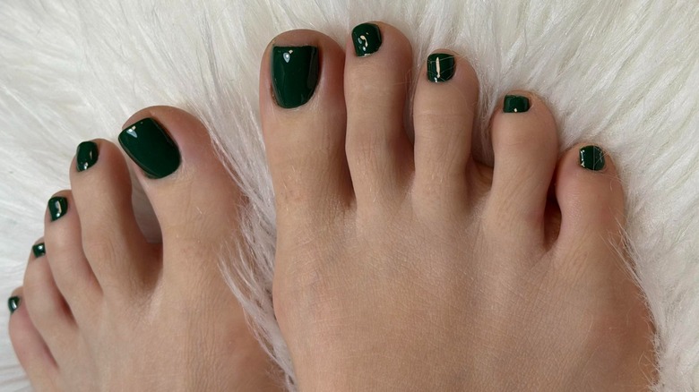 Two feet on a fluffy blanket with a dark green pedicure