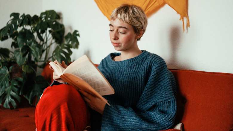 A woman with short hair reading a book on a red couch