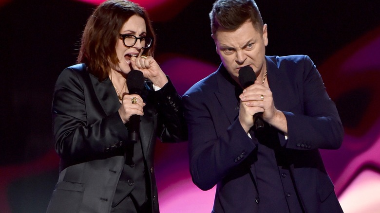 Megan Mullally wearing a black blazer and Nick Offerman wearing blue suit with a gold necklace