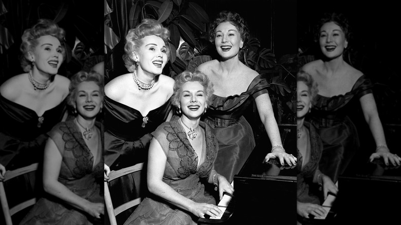 Zsa Zsa Gabor (L) and Magda Gabor (R) stand and smile behind a sitting Eva Gabor (C)