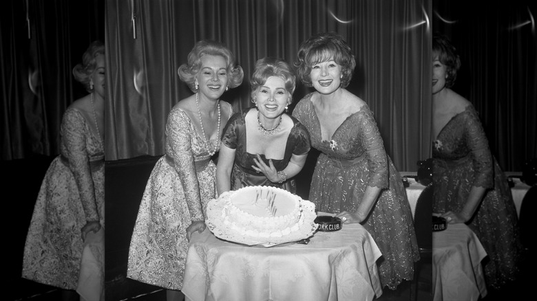 Eva Gabor (L), Zsa Zsa Gabor (C), and Magda Gabor (R) smile behind a birthday cake