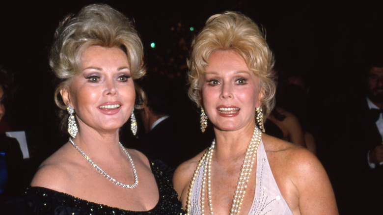 Zsa Zsa Gabor (L) smiles wearing diamond earrings next to Eva Gabor (R) wearing a layered pearl necklace
