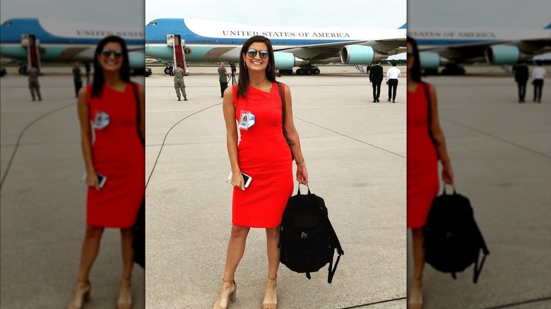 Kaitlan Collins smiles in front of a plane wearing an orange neon dress and sunglasses