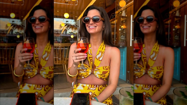 Kaitlan Collins smiles wearing brown sunglasses and a patterned yellow co-ord