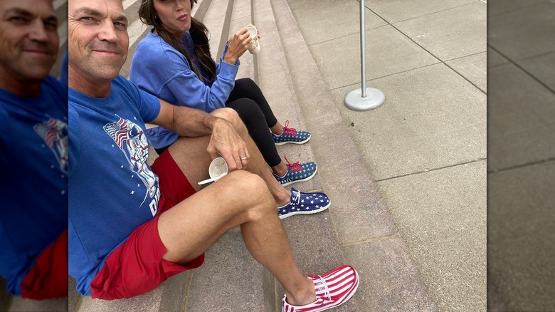 Bryon Noem and Kristi Noem sitting together on steps while he smiles and her head is cut off the image