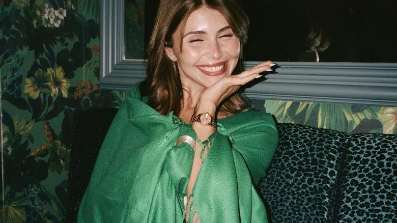 Olivia Jade smiles and poses for a photo on a couch in front of floral wallpaper