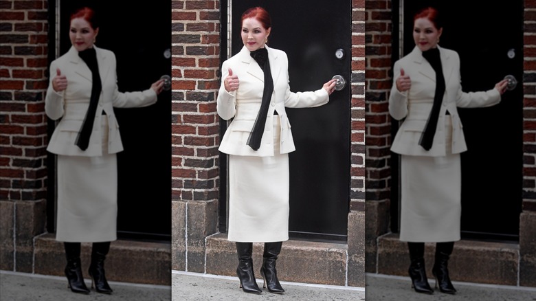 Priscilla Presley flashing a thumbs up while wearing a white skirt suit