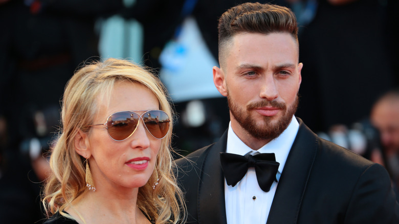 Sam Taylor-Johnson smiles with sunglasses next to Aaron Taylor-Johnson in a suit