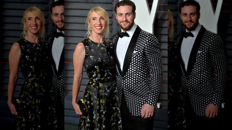 Sam Taylor-Johnson smiles in a floral maxi dress next to Aaron Taylor-Johnson in a grey and black psychedelic blazer