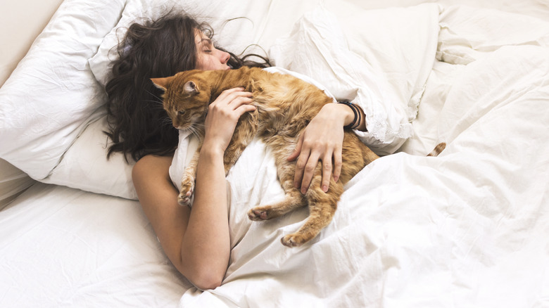 Woman cuddles with cat in bed