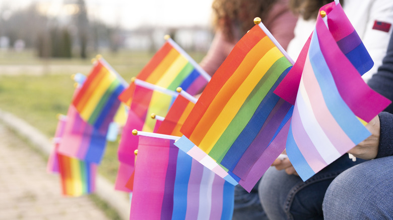 People hold multiple types of mini Pride flags in their hands