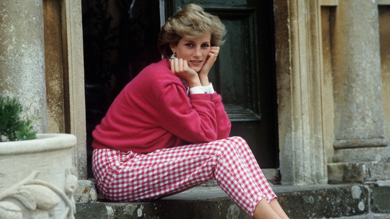 Princess Diana sitting on a step in a pink sweater and checkered pants in 1986