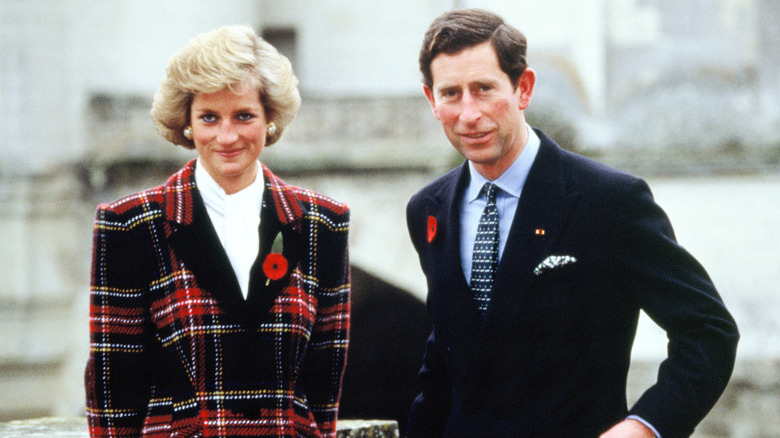 Princess Diana wearing red-featuring plaid and a floral brooch while posing next to Charles III