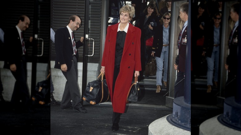 Princess Diana wearing a long red coat while carrying bags at an airport