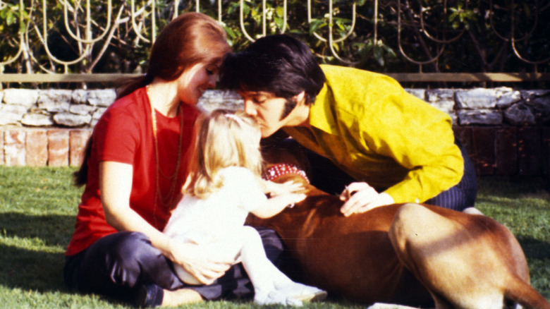 Elvis Presley kisses Lisa Marie Presley on the head while she is sitting on Priscilla Presley