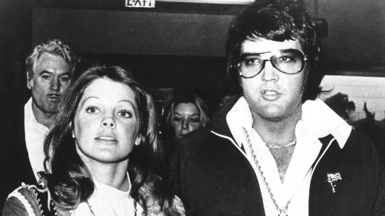 Priscilla Presley holds hands with Elvis Presley wearing glasses