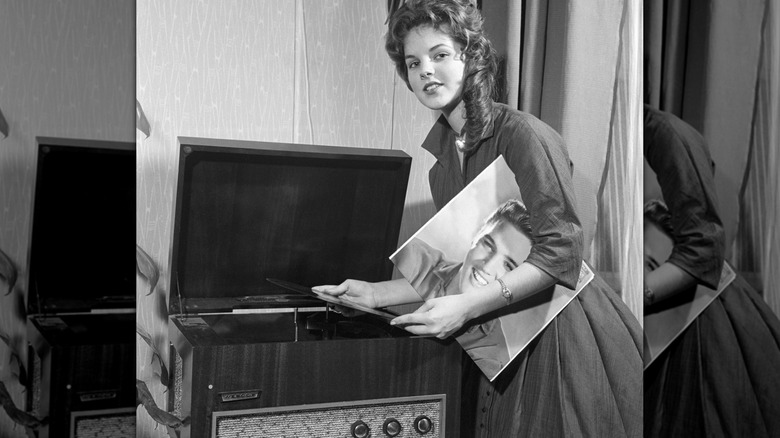 Priscilla Presley holding an Elvis Presley vinyl looking at the camera