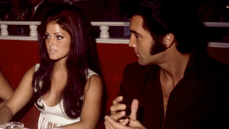 Priscilla Presley with long red hair sits next to Elvis Presley with black sideburns