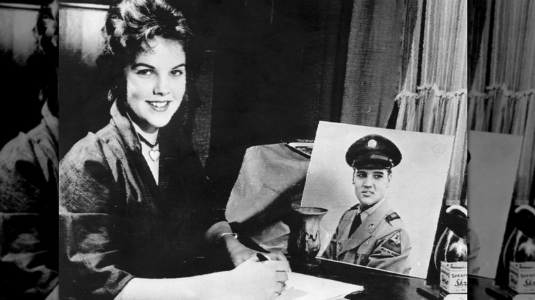 A black-and-white photo of Priscilla Presley writing a letter to Elvis Presley in 1960