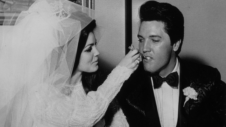 A black-and-white photo of Priscilla Presley feeding Elvis Presley a piece of wedding cake on their wedding day