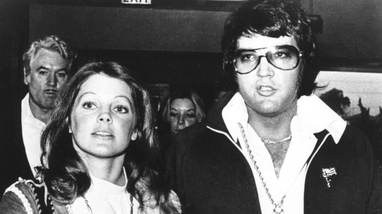 A black-and-white photo of Priscilla Presley and Elvis Presley leaving a divorce hearing together in 1973