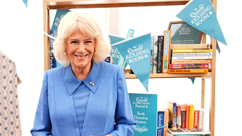 Queen Camilla smiling next to a bookshelf with multiple books at 