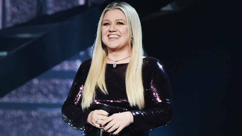 Kelly Clarkson smiling in a black sequin dress while on stage