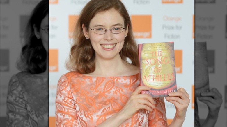 Madeline Miller holds up her book while smiling