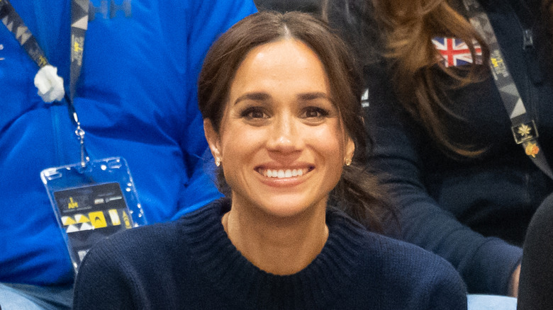 Meghan Markle smiling at the Invictus Games wearing a blue sweater