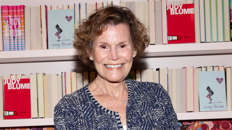 Judy Blume standing in front of a bookshelf with her books
