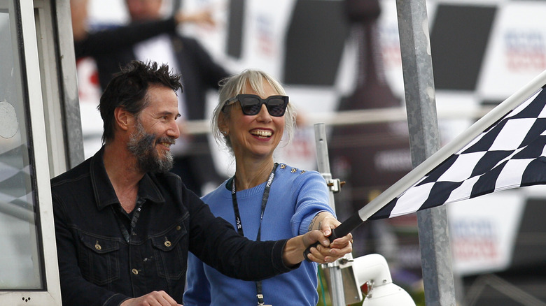 Keanu Reeves and Alexandra Grant wave the checkered flag at the MotoGP of Germany at the Sachsenring Circuit on July 07, 2024