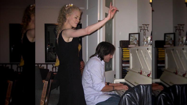 Keith Urban playing the piano while a curly-haired Nicole Kidman dances behind him