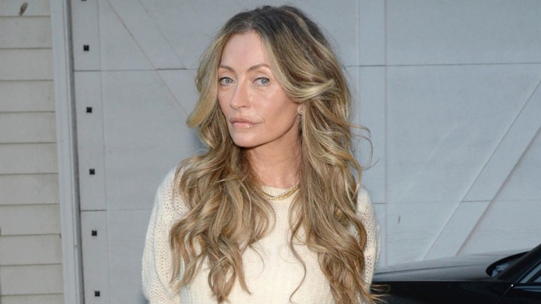 Rebecca Gayheart posing with a neutral expression outside in a cream, knit sweater