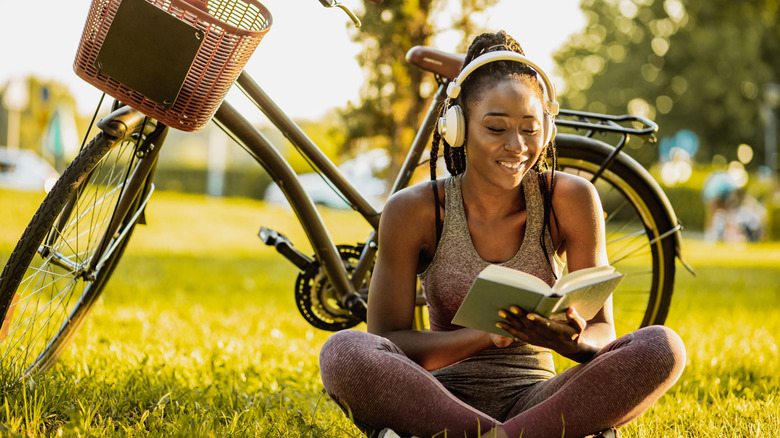 Photo of a young African American woman is wearing wireless headphones; she is sitting on the grass next to her bicycle