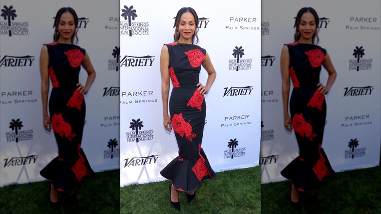 Zoe Saldana posing with a hand on her hip while wearing a black, figure-hugging gown with a flared skirt