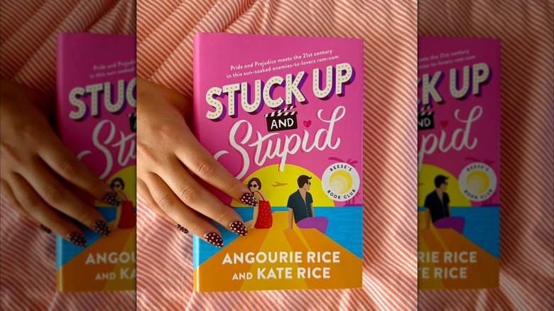 A hand holding Stuck Up And Stupid by Angourie Rice and Kate Rice