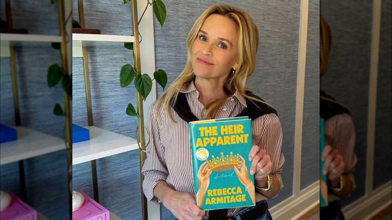 Reese Witherspoon holding a copy of The Heir Apparent by Rebecca Armitage