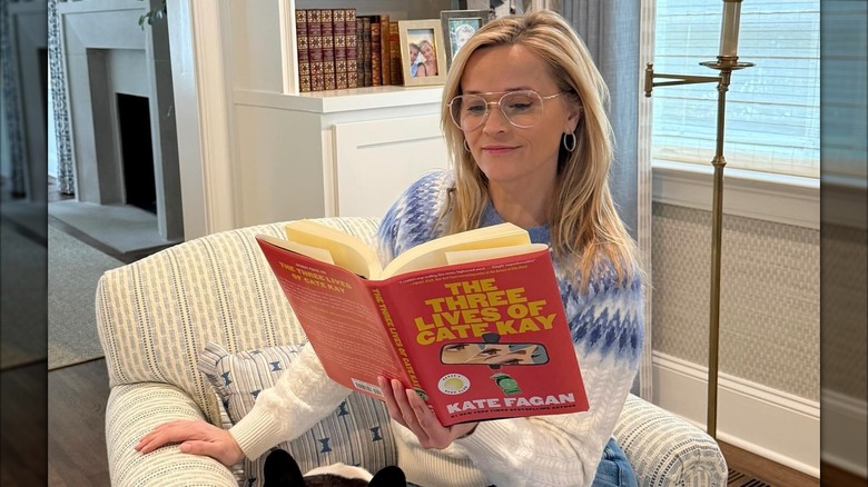 Reese Witherspoon holding The Three Lives of Cate Kay by Kate Fagan